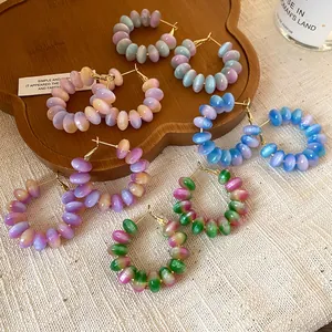 Close-up of colorful gradient resin bead hoop earrings displayed on a rustic wooden tray.