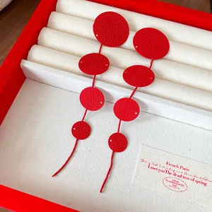 Close-up of elegant red circular textured tassel earrings displayed in a premium jewelry box
