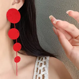 Close-up detail of stylish red circular textured metal tassel earrings on model
