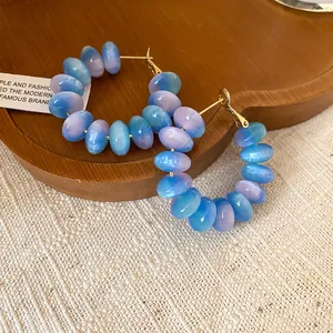 Macro view of translucent blue and purple resin beads on silver needle hoop earrings.