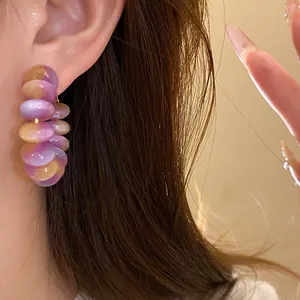 Close-up view of stylish purple and amber resin hoop earrings worn on an ear