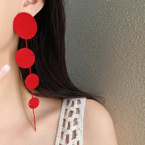 Close-up detail of long red textured circular tassel earrings worn by a model against dark hair.