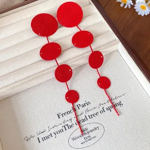 Detailed view of red textured round disc tassel earrings in a wooden jewelry box