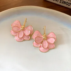 Close-up of elegant pink enamel flower earrings with gold-toned details and silver needles.