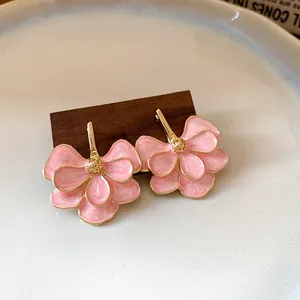 Close-up of pink enamel flower earrings with gold-plated edges on a wooden stand