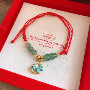 Close-up of woven red string bracelet with green beads and blue rocking horse charm