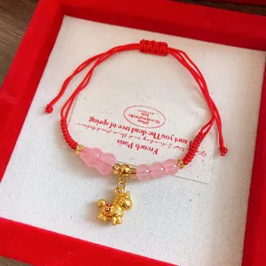Detailed view of a red braided rope bracelet with pink glass beads and golden pony pendant
