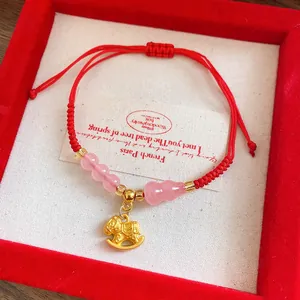 Detail of red braided rope bracelet with pink beads and a golden rocking horse charm
