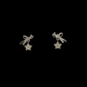 Detailed view of silver bow earrings with zircon star dangles on black background