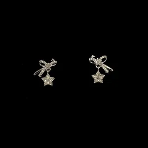 Detailed macro view of silver bow stud earrings with sparkling star charms on black background