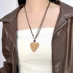 Close-up of bohemian woven heart pendant necklace on model wearing a brown jacket