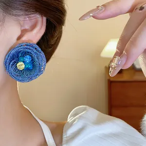 Nahaufnahme eines großen blau gewebten Blumenohrsteckers mit leuchtenden Kristallen