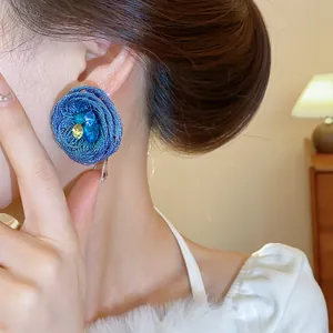 Nahaufnahme von blau gewebten Blumenohrringen mit Kristallen getragen von einem Model