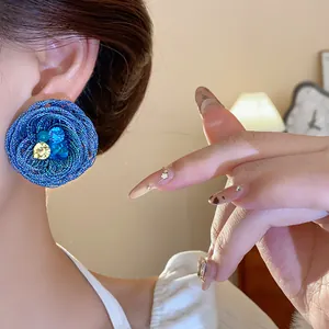 Detaillierte Nahaufnahme eines blauen gewebten Blumenohrrings mit Kristallen am Model