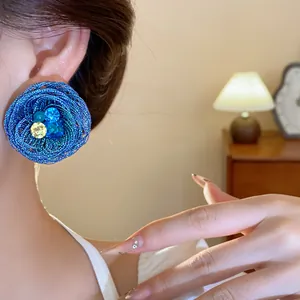 Detailansicht eines blauen gewebten Blumenohrsteckers mit glitzernden Kristallen