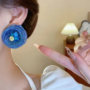 Nahaufnahme eines blau geflochtenen Blumen-Ohrsteckers mit Strasssteinen am Ohr