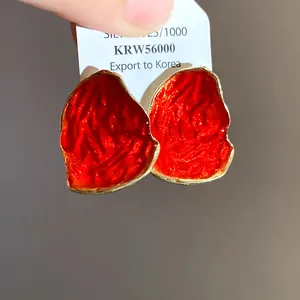 Dettaglio di orecchini a perno in smalto rosso irregolare con bordo dorato e ago in argento