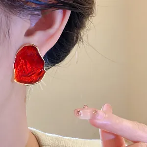 Primo piano di orecchini ovali irregolari in smalto rosso retrò indossati da modella