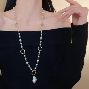 Model wearing long gold chain necklace with irregular faux pearls over black sweater
