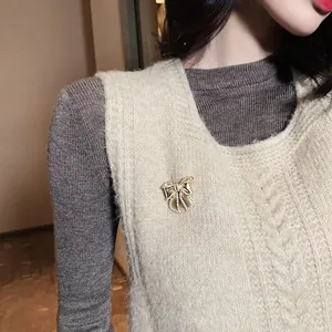 Elegant vintage-style golden bowknot brooch with delicate pearls on a beige knitted vest