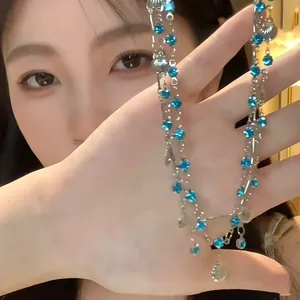 Close-up of a double-layered necklace with blue crystals and shells held by a model.