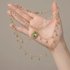 Macro view of a gold-tone double-layer necklace featuring green gemstone and shell fringes