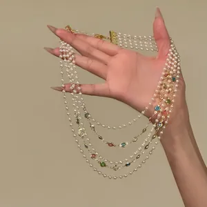 Detailed view of a multi-layer pearl necklace with colorful gemstone accents on a hand.