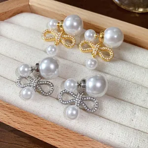Primo piano di eleganti orecchini a fiocco in oro e argento con perle sintetiche.