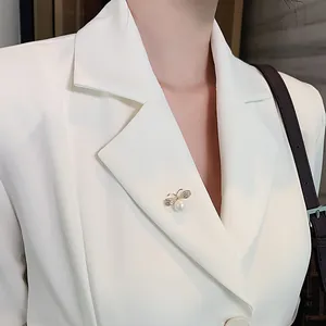 Close-up detail of an elegant retro butterfly pearl brooch pinned to a white blazer lapel.