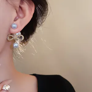 Dettaglio ravvicinato di eleganti orecchini a fiocco placcati oro con perle sulla modella.