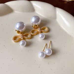 Dettaglio ravvicinato di orecchini a fiocco placcati oro con perle su un piatto.