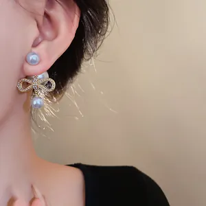 Primo piano di eleganti orecchini a fiocco placcati in oro con perle finte sull'orecchio