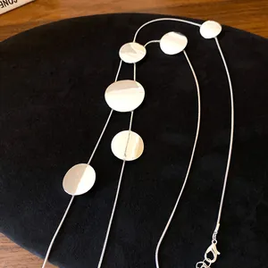 Detail view of a minimalist silver necklace with flat circular disks on black velvet
