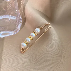 Detailed view of elegant safety-pin brooch with four pearls and rhinestones on beige fabric.