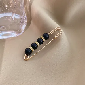 Close-up detail of a vintage gold safety pin brooch with black beads and crystal rings