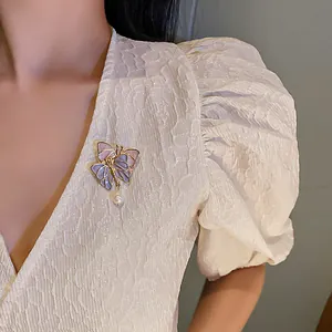 Close-up of elegant butterfly brooch with pearl pendant on textured white puff sleeve top