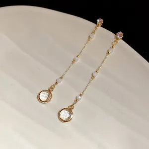 Elegante goldene Quastenohrringe mit runden Glasanhängern auf weißer Keramikoberfläche
