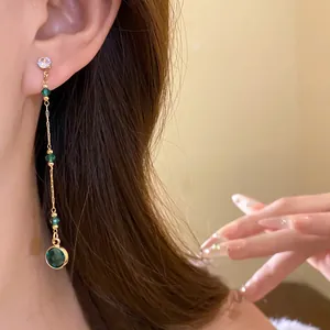 Detailansicht eines eleganten langen Quastenohrrings mit grünen Glasperlen am Ohr des Modells.