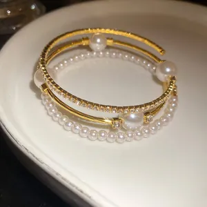 Close-up of elegant three-layer gold bracelet featuring lustrous pearls and sparkling rhinestones