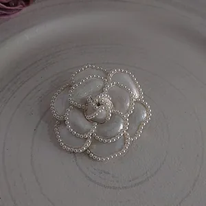 Detailed view of elegant white enamel camellia flower brooch with decorative pearl trim