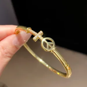 Close-up of 18k gold plated bangle with a sparkling zircon cross and peace symbol