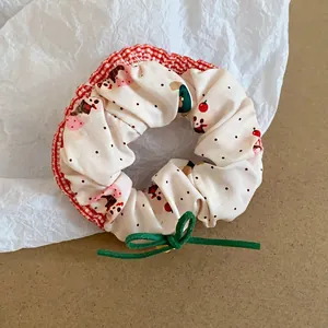 Close-up of a cream floral scrunchie with red checkered trim and green bow detail