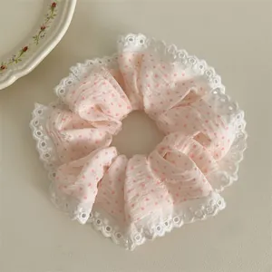 Close-up of a pink polka dot fabric scrunchie with delicate white lace trim detail