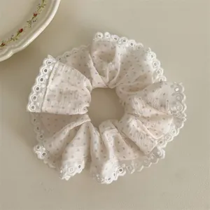 Close-up of a white fabric scrunchie with blue polka dots and delicate lace trim detail