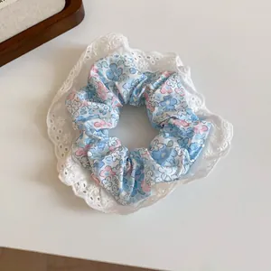 Detailed view of floral scrunchie with delicate white lace trim and blue floral print.
