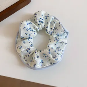 Detailed macro view of a white fabric scrunchie featuring an elegant blue floral print pattern.