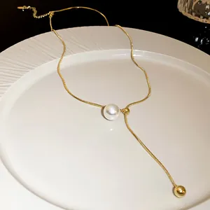 Close-up of adjustable gold snake chain necklace with pearl and bead tassels on white plate