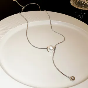 Detailed macro view of an adjustable silver snake chain necklace with a pearl tassel
