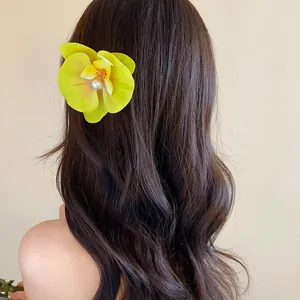 Détail d'une pince à cheveux orchidée jaune avec perle sur cheveux châtain ondulés