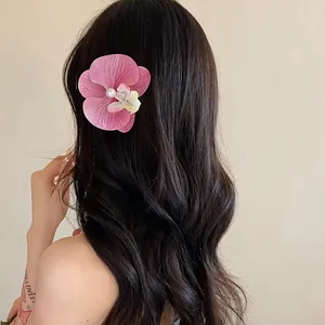 Élégante pince à cheveux orchidée rose avec perle sur de longs cheveux noirs ondulés